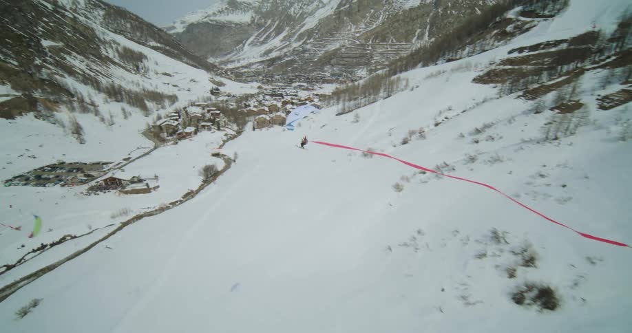 A glider with a parachute on flying through the air above a snowy covered range