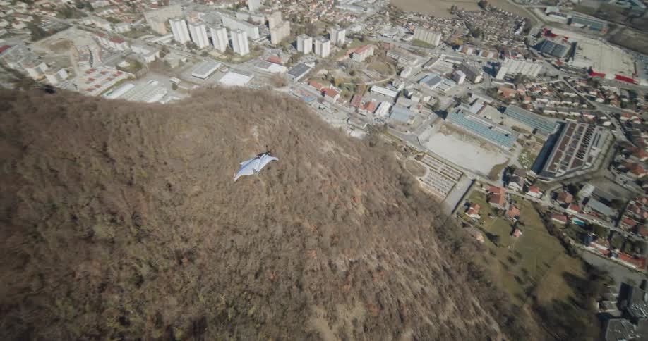 A person wingsuit flying over a mountain side with a city in the distance