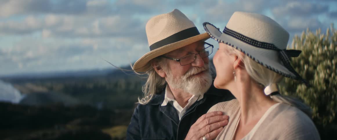 Happy older couple kissing on mountain top on windy day