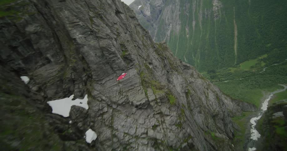 A person paraglides over a river in a mountain range