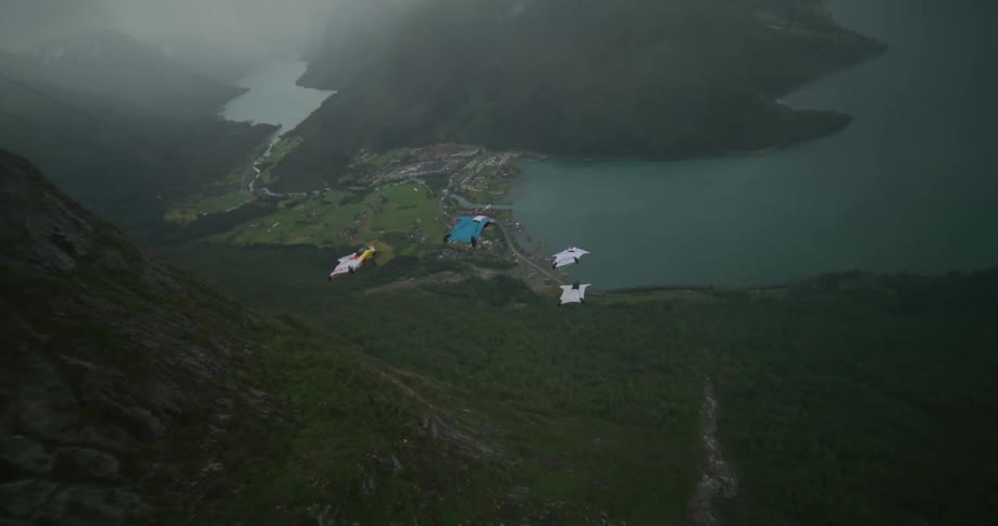Four people in gliding suits jump off a cliff and fly through the air