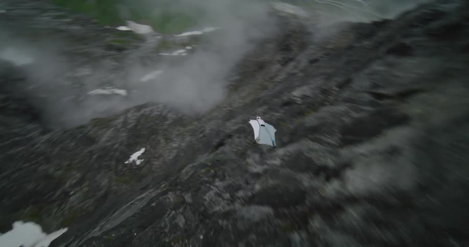 A man wearing a parachute suit jumps off a cliff and glides in the air