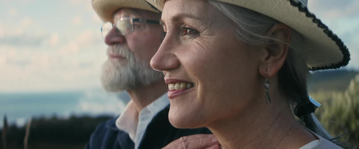 A man and a woman wearing hats are relaxing outside and she has a big smile on her face