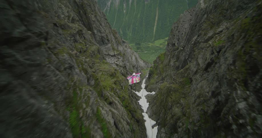Person wearing wing suit jumps off cliff over ice filled crevice and glides across landscape