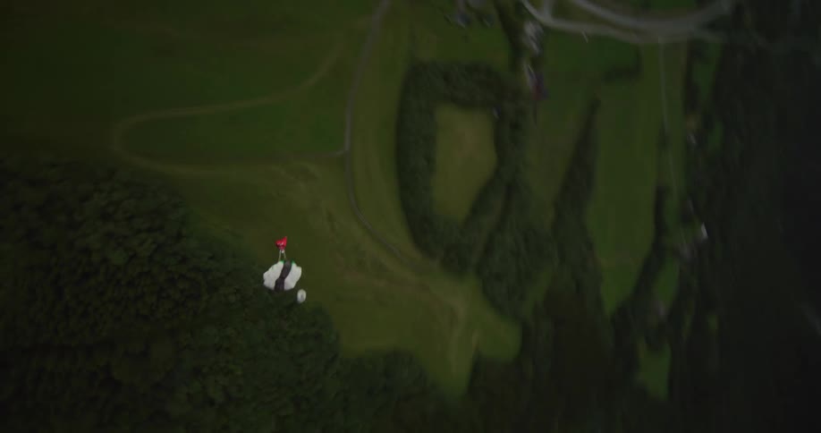 A person wearing a wingsuit is flying over a mountain river valley as they open their parachute