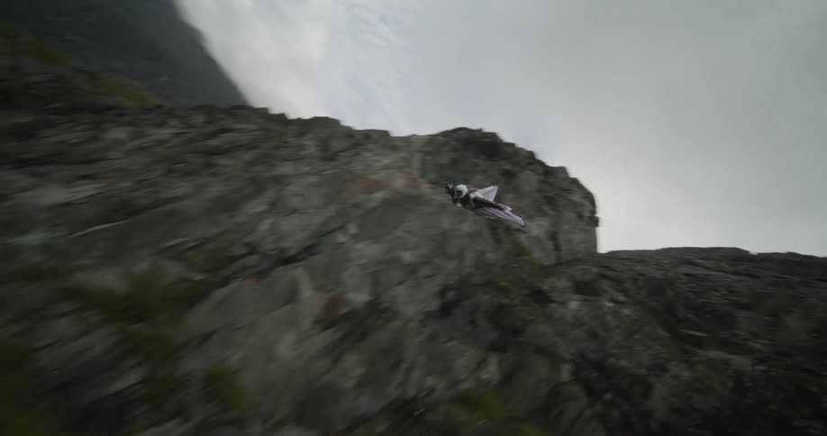 Two people paragliding jump off a cliff and glide above the land