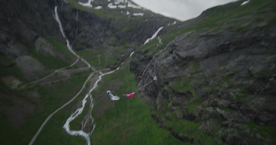 A person wearing a wingsuit is flying over a mountain river valley as they open a parachute