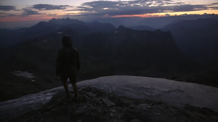 A person is standing on the edge of a cliff at dawn