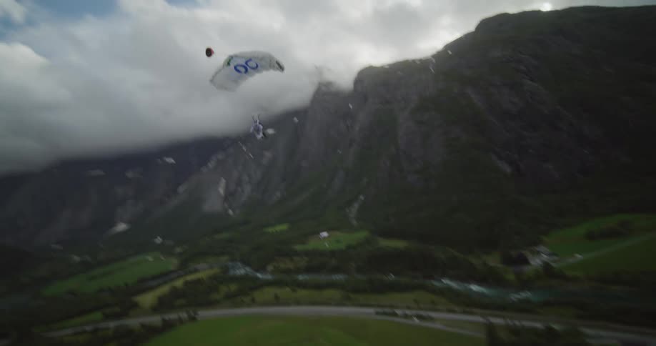 A paraglider is flying near mountains and a road through a river valley