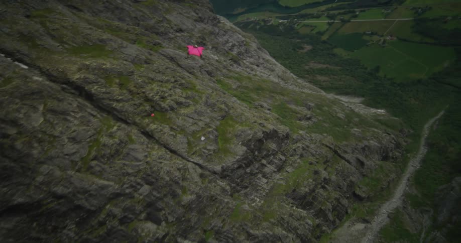 A glider in a pink suit flying through the air above a rocky mountain range