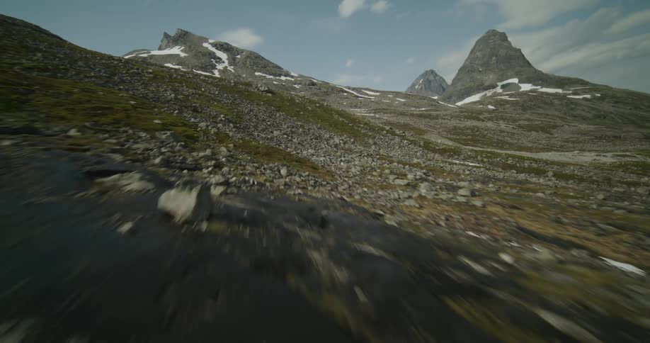 Moving across a rough terrain scattered with rocks there are mountains in the distance under a cloudy sky