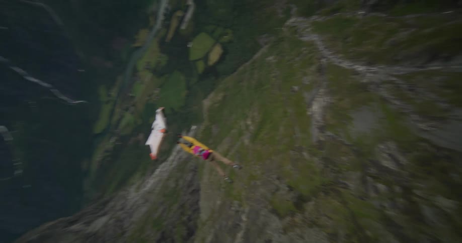 Two people jumping off a mountain edge and gliding with a wingsuit