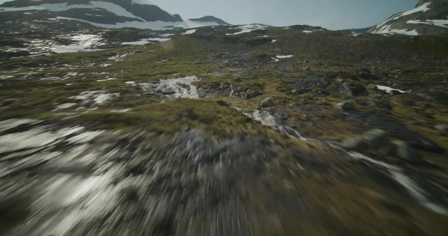 A sped up aerial of a mountain range that is rocky with water flowing down