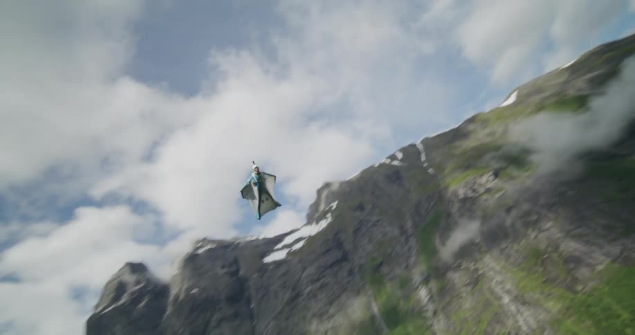A person wearing a wingsuit is flying over a mountain valley as they open their parachute