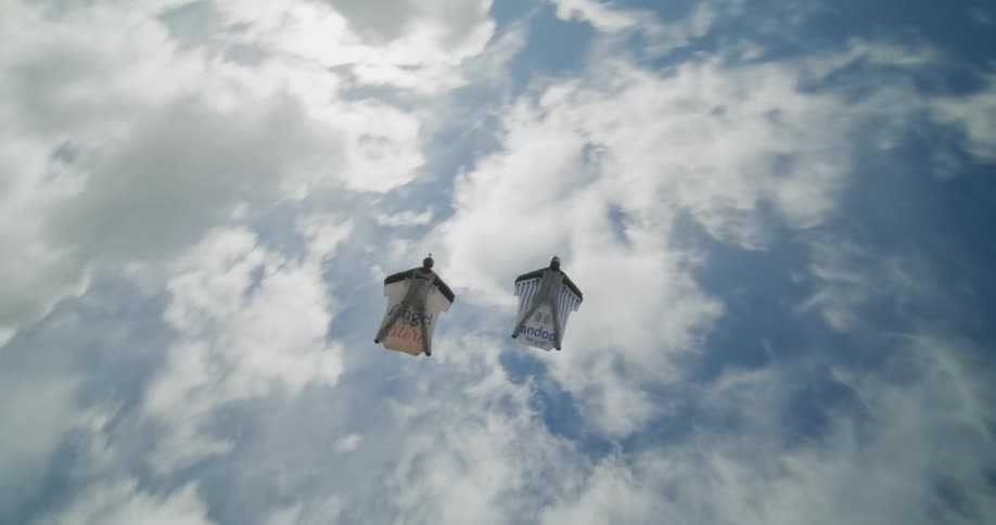 Two gliders in white suits free falling through a lush green valley
