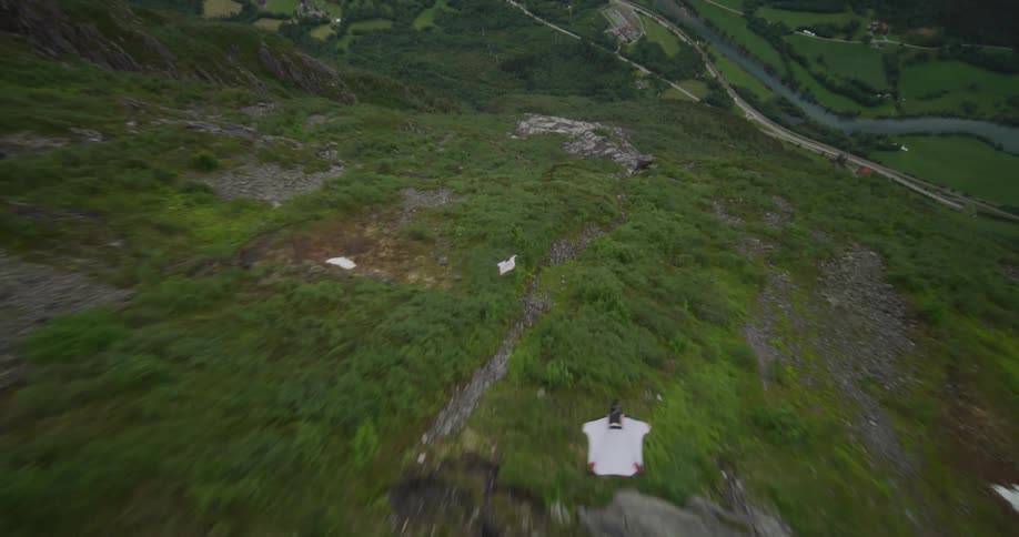 Two people in gliding suits glide down a rocky mountainside