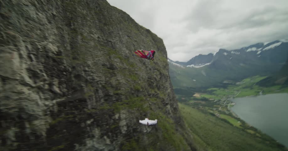 Two people wearing wing suits fly over a canyon