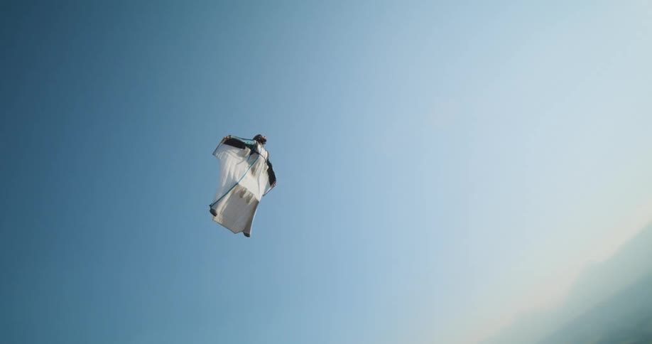 A person in a white suit gliding through the air above a small town