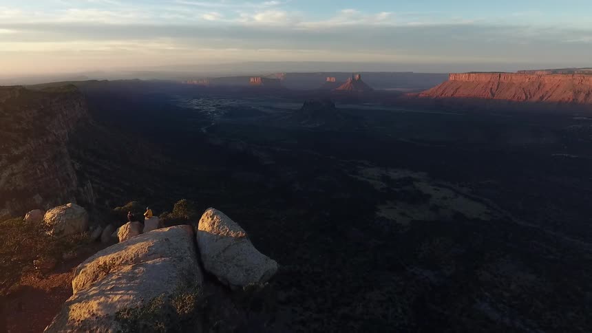 Two people sit on some rocks overlooking a huge canyon