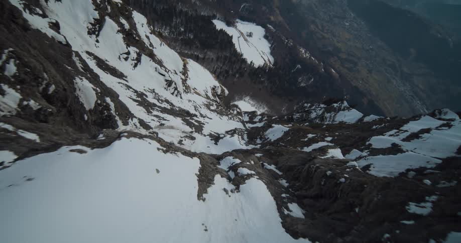 Mountains laced with snow and steep rocky cliffs with surrounding trees under a hazy sky