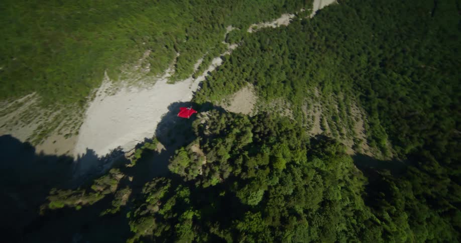 A person in a red suit gliding through rocks and mountains and above lush green valleys
