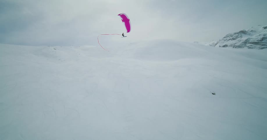 A person paraglides over a snowy mountain range