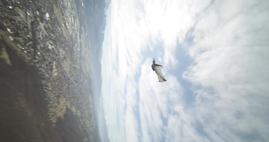 A person in a white suit gliding through the air above a forest of dead trees
