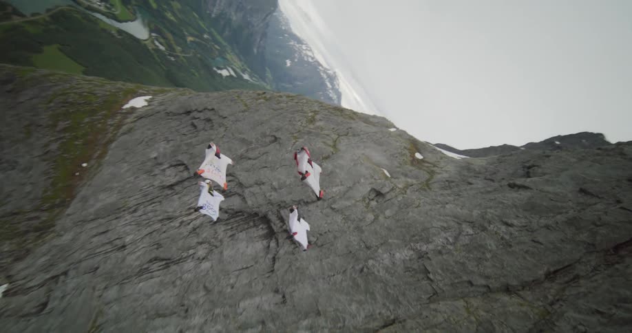 Four people gliding through the air above rocky mountains