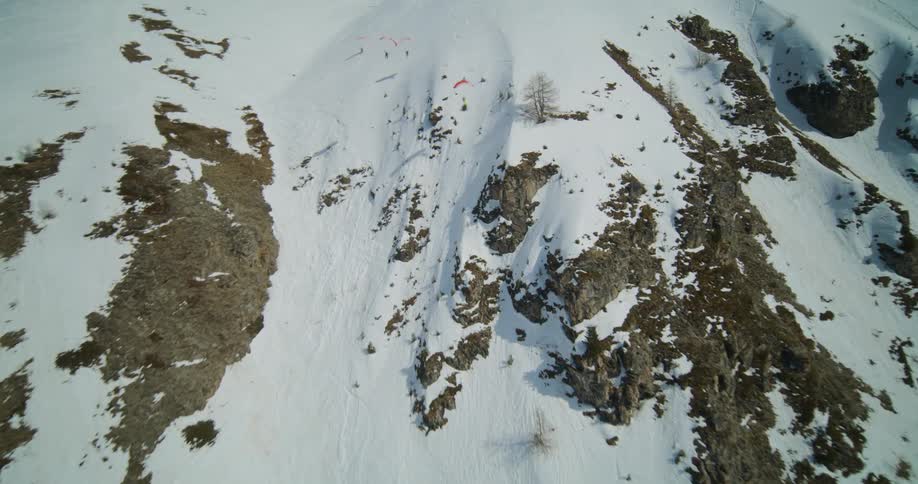 A group of paragliders soar down a mountain