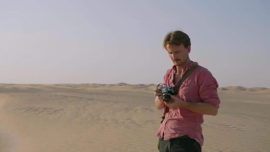 A man standing in sand dunes is taking pictures