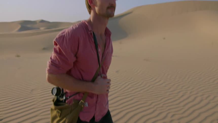 A man carrying a camera is walking in the desert