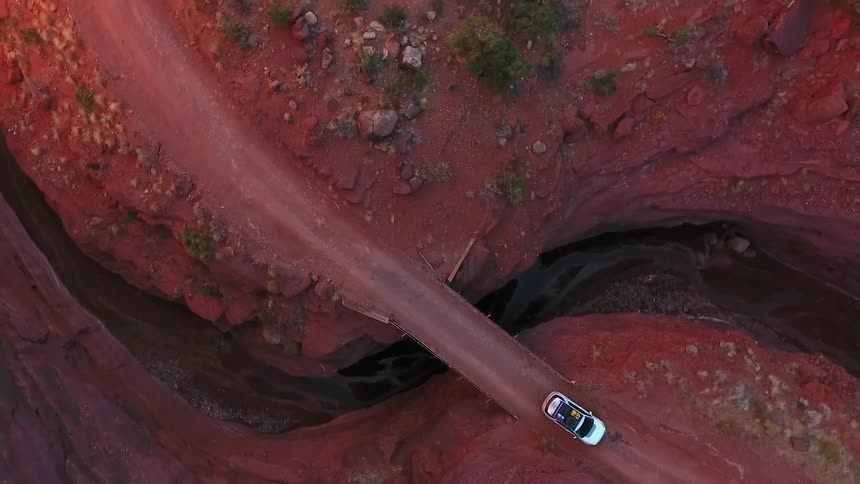 An suv drives over a short, narrow bridge in a desert landscape