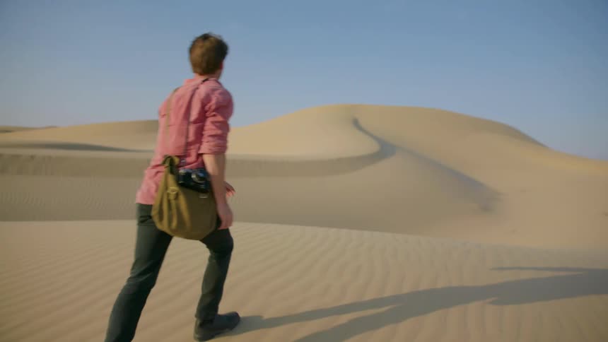 Man carrying his camera and equipment through a desolate sandy area