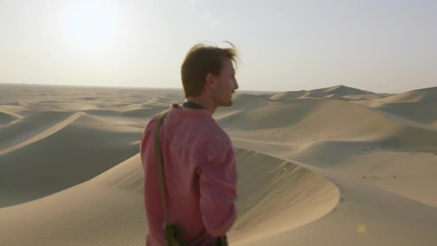 A man puts a camera on on his shoulder in the desert