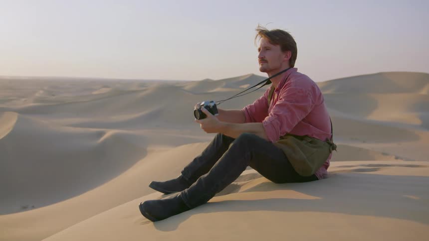 Man sitting in the middle of a desert taking pictures