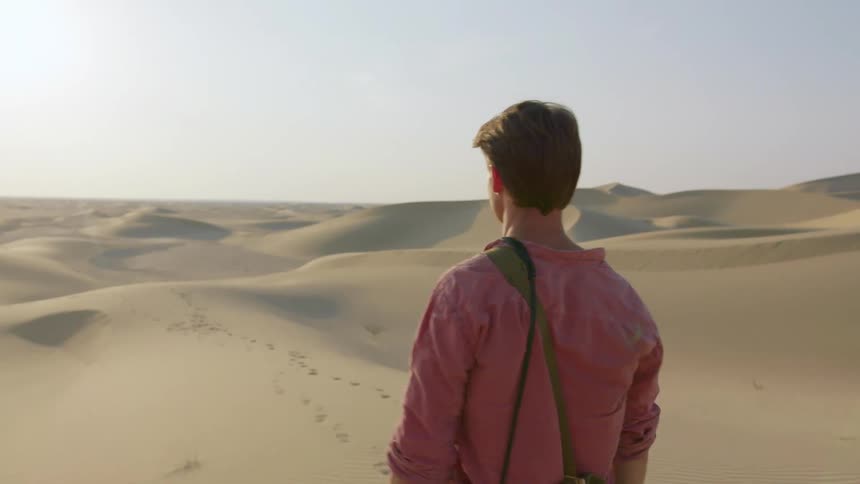 Man carrying his camera and equipment through a desolate sandy area