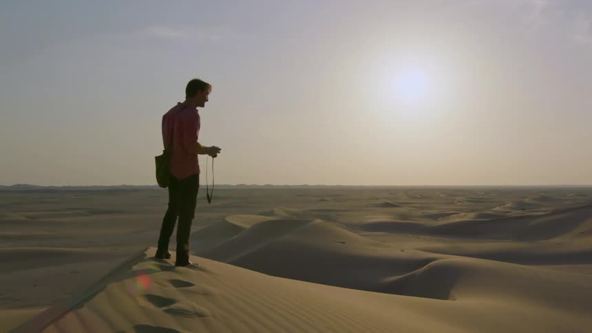 A man stands on a sand dune at sunset
