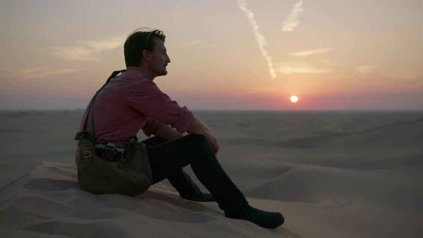 Man sitting in sand observing the dunes as sun sets