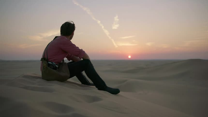 Man sits in the middle of the desert at sunset