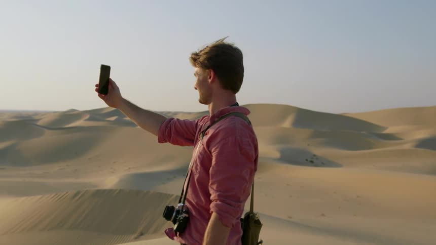 A man standing on sand dunes laughs and talks on his phone