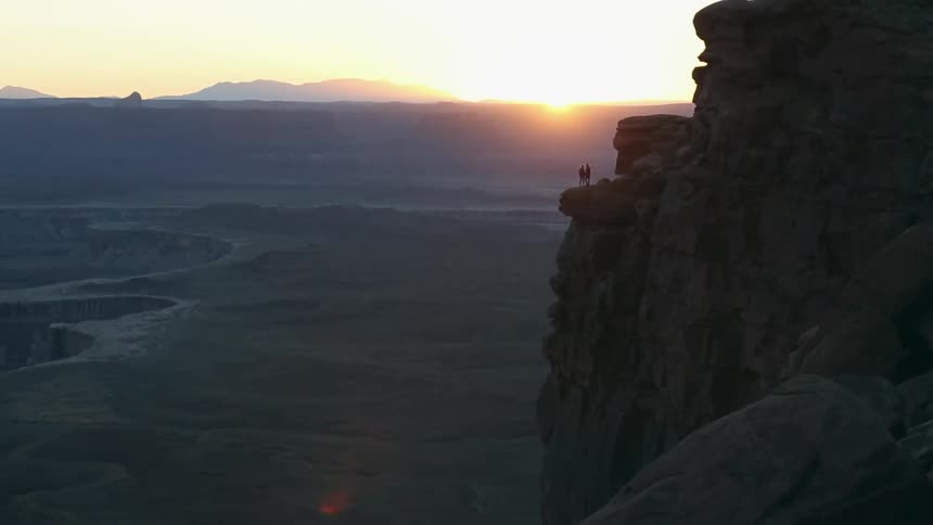 Two people stand on a cliff at sunrise