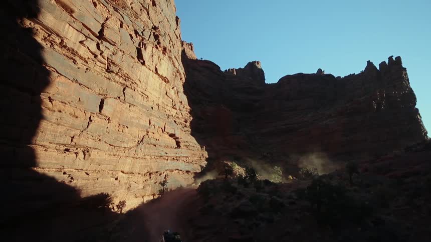 A car drives down a dirt road by a canyon