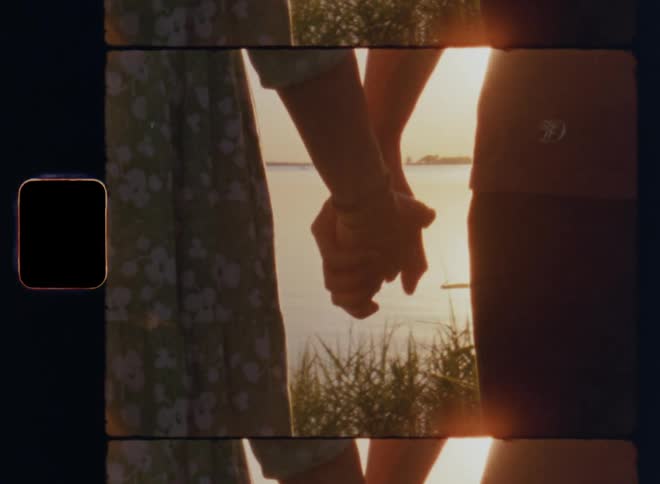Ms of hands joining as young couple stands together during a romantic date watching the sunset over a lake on vintage 8mm film with a nostalgic vibe