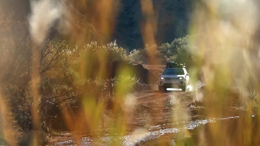 A vehicle is driving on hills and over streams