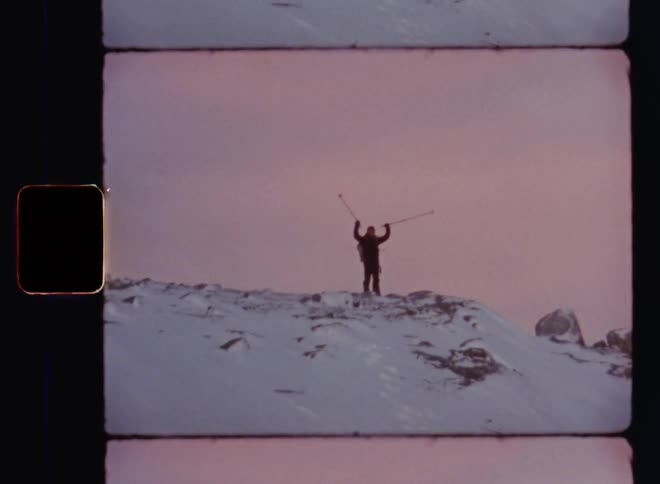 Sporty or athletic person holding ski or hiking poles standing cheering on a mountain top peak or summit celebrating achievement of a challenging ascend in cold and harsh conditions with deep snow and freezing temperatures during beautiful winter evening