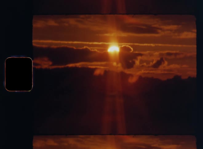 Dynamic handheld 8mm wide shot of sun setting or rising behind the clouds in a sepia toned sky behind the silhouette of trees at the horizon during golden hour