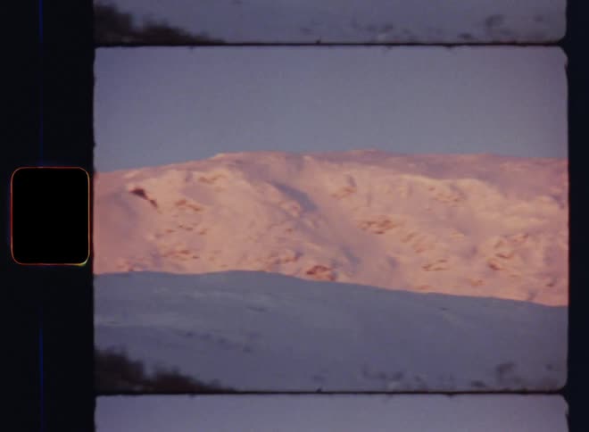 Handheld dynamic 8mm film footage of a snowy mountain landscape during wintertime in a rural area with pristine and untouched nature and wild forest with birch trees without leaves on a freezing cold November day at the beginning of winter