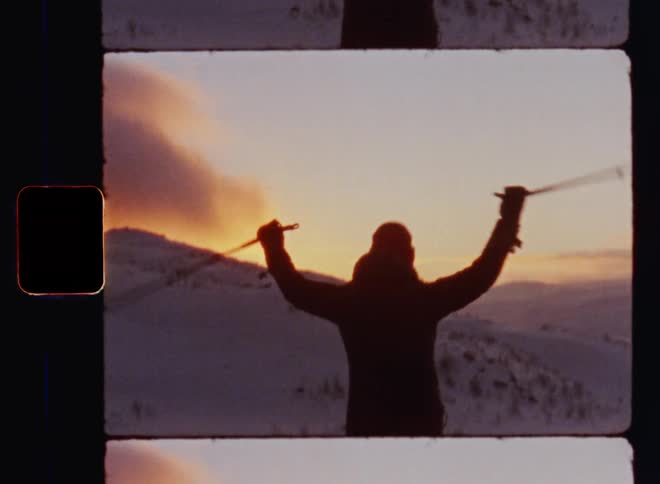 Silhouette of a person cheering and raising the arms while holding ski poles after hiking or skiing up the mountain and reaching the peak or summit in the evening light during sunset celebrating the successful ascend and reaching a challenging goal