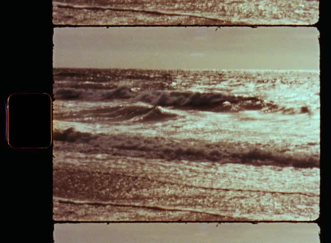 Old footage of the ocean or sea as waves are rolling in and washing up the beach as the bright sun shines from the rear and the water moves symbolizing the power of Mother Nature and the elements