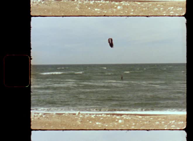 A sportive person kite surfing on the ocean or sea as waves roll into shore and wash up on the beach while the athlete is enjoying water sports and outdoor activities using the energy of the wind to move dynamically at high speed